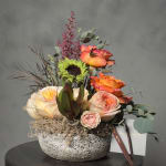 Mixed floral arrangement in a textured bowl with peach and orange roses