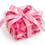 Clear gift box filled with pink rose petals and tied with a pink ribbon
