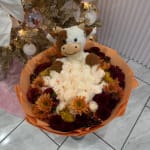 Bouquet of cream roses and orange chrysanthemums with a plush cow topper