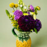 Purple and white flowers arranged in a pineapple-shaped ceramic pitcher