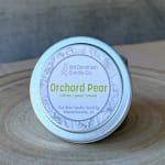 Small tin candle labeled Orchard Pear on a wooden surface