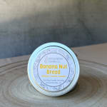 Small tin candle labeled Banana Nut Bread on a wooden surface