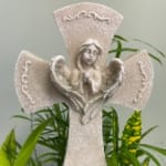Decorative angel figurine with a cross-shaped design and greenery behind it