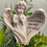 Angel figurine with a heart-shaped plaque and flowers behind it