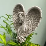 Angel statue above green foliage and yellow flowers