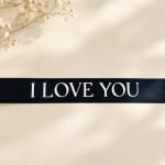 Black ribbon with "I LOVE YOU" text beside small white flowers
