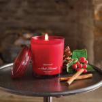 Red candle in a glass jar with pinecones and berries on a tray