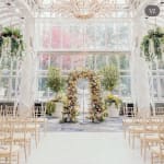 Floral wedding arch in a bright glass conservatory with rows of chairs