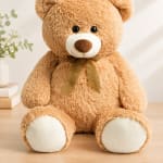 Large teddy bear with a ribbon sitting beside a small vase of flowers