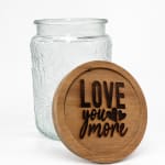 Clear glass jar with a wooden lid engraved "Love you more"