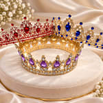 Two jeweled crowns on a satin cushion with small white flowers nearby