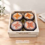 Wooden crate holding four labeled food jars on straw filler