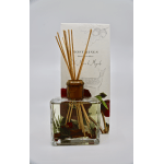Square glass reed diffuser bottle with botanical accents and packaging behind it