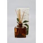 Amber reed diffuser bottle with wooden sticks in front of an illustrated box