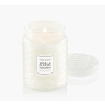 Lit white candle in a textured glass jar with a lid beside it
