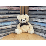 Cream teddy bear with a dark ribbon bow sitting against a wooden backdrop