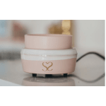 Pink cosmetic jar with a gold heart logo on a counter