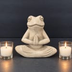 Stone frog statue in a meditative pose with two lit candles on either side