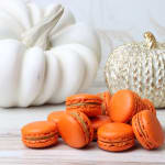 Orange macarons arranged in front of decorative white and gold pumpkins