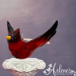 Red glass bird ornament with black wings and yellow beak on a white pedestal