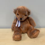 Brown teddy bear with a ribbon sitting on a wooden surface