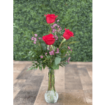Three red roses in a clear glass vase with small pink filler flowers