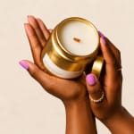 Hands holding a gold candle jar with a white wax top