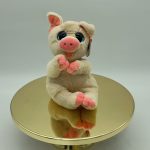 Plush pig toy with pink accents sitting on a gold mirrored stand