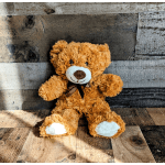Fluffy brown teddy bear with a ribbon sits on a rustic wooden surface