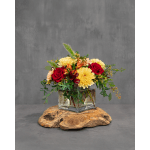 Red roses and yellow mums in a clear square vase on a wood slab