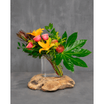 Tropical bouquet with yellow lilies, pink roses, and red protea in a glass vase