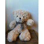 Cream teddy bear with a plaid ribbon sitting on a wooden surface