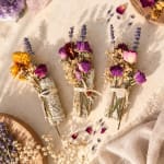 Three small dried flower bundles tied with twine on a light fabric surface.