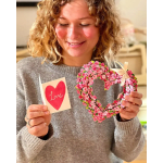 Person holding a red heart love card and a pink flower-covered heart wreath