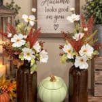 Two autumn floral arrangements in brown bottles with a pumpkin container between them