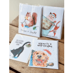 Four Christmas greeting cards with illustrated animals on a wooden surface