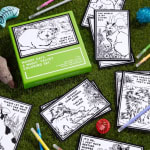 Cat-themed coloring set with black-and-white cards and colored pens on grass