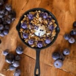 Skillet filled with granola and blueberries on a wooden table
