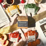 Assorted tea packets arranged with peaches and a magazine on a cloth surface.