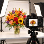 Mixed bouquet in a glass vase on a studio table with a camera in front