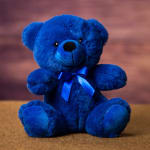 Blue teddy bear with a ribbon bow sitting on a surface