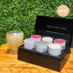 Gift box with six tea tins beside a glass of iced tea