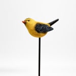 Yellow bird figurine on a black stake against a white background