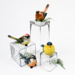 Decorative bird figurines on clear glass blocks with fern sprigs