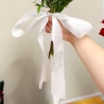 Hand holding a flower stem tied with a large white ribbon bow