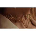 Gold heart-shaped necklace with green stones worn on a person's neck