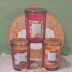 Three scented candles in glass jars arranged before a glittery pumpkin backdrop.