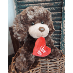 Brown teddy bear holding a red heart tag in a wicker basket