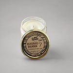 Glass jar candle with a labeled metal lid on a plain background