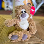 Plush teddy bear sitting on a wooden surface with a gift tag